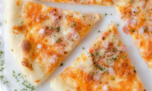 Kawałki pysznej pizzy bez drożdży z ciągnącym się serem, szynką i cebulką, posypane świeżym tymiankiem.