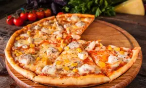 Pyszna pizza z kurczakiem i kukurydzą, podana na drewnianej desce, z pomidorkami koktajlowymi i bazylią w tle.