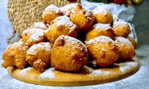 Puszyste pączki z serków homo, posypane cukrem pudrem, wyglądają jak śnieżne kule na drewnianej desce.