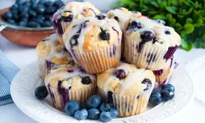 Stos puszystych muffinek z borówkami i białą czekoladą, polanych lukrem, ozdobiony świeżymi borówkami.