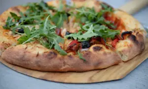Puszyste ciasto pizzy z rukolą, oliwkami i papryką, podana na drewnianej desce.