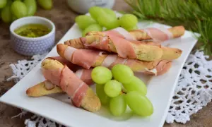Grissini z szynką parmeńską, zielone winogrona i sos na talerzu. Idealna przekąska na przyjęcie.