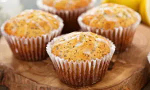 Cztery muffinki cytrynowe na oleju, posypane makiem i polane lukrem, prezentują się apetycznie na drewnianej desce.