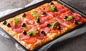 Chrupiąca pizza na cieście francuskim z salami, pomidorami i oliwkami, udekorowana listkami bazylii.
