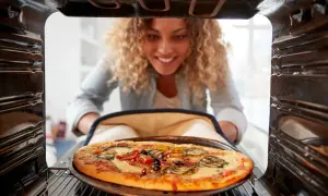 Kobieta wyjmuje z piekarnika upieczoną pizzę z warzywami i oliwkami.