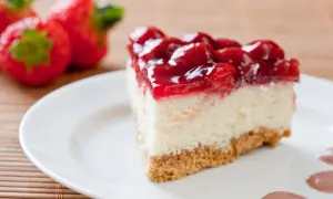 Pyszny sernikobrownie z truskawkami na białym talerzu, obok świeże truskawki.