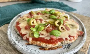 Mini pizza z serka wiejskiego, z sosem pomidorowym, oliwkami, kiełbaską i bazylią, na talerzu.