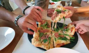 Ręce sięgają po kawałki pysznej pizzy na kamieniu w piekarniku, ciągnący się ser i rukola.