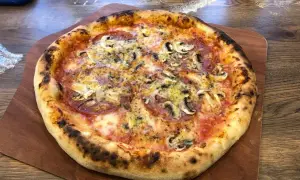 Pyszna pizza na drewnianej desce, idealnie wypieczona. Zastanawiasz się, ile nagrzewa się kamień do pizzy, by uzyskać taki efekt?