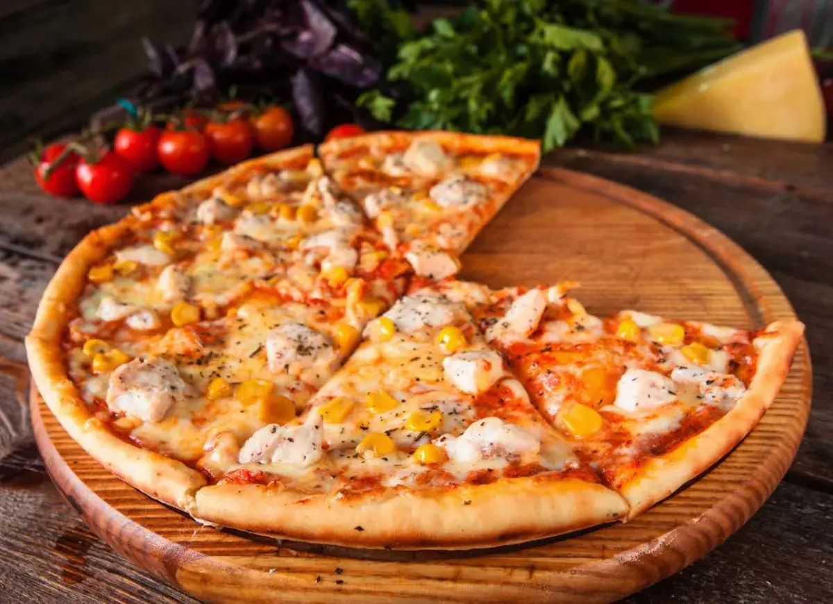 Pyszna pizza z kurczakiem i kukurydzą, podana na drewnianej desce, z pomidorkami koktajlowymi i bazylią w tle.