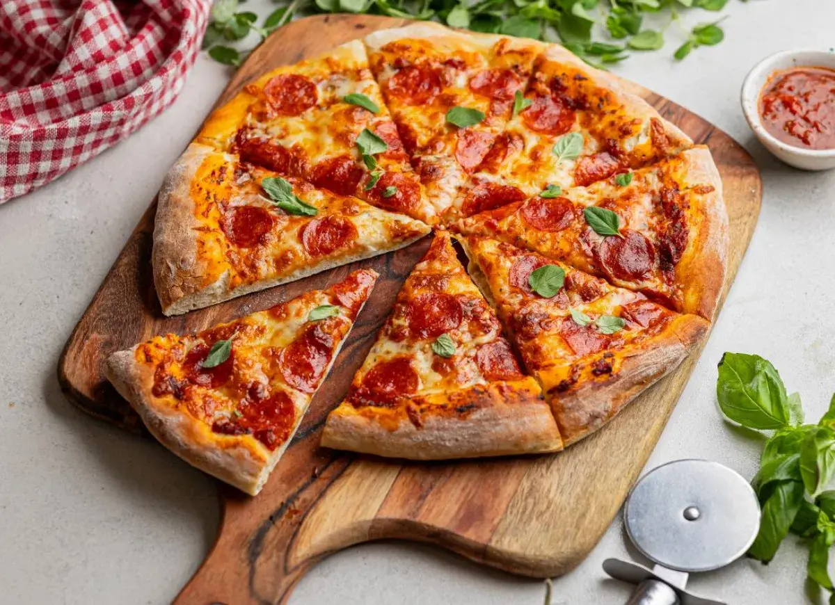 Pyszna pizza z pepperoni, z ciągnącym się serem i świeżą bazylią, podana na drewnianej desce.