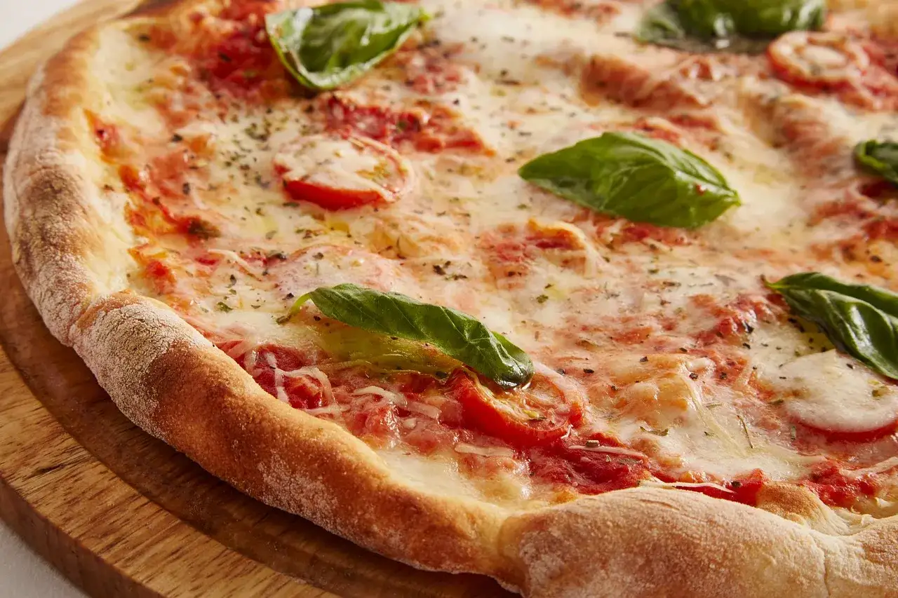 Pyszna pizza bez drożdży z pomidorami, mozzarellą i świeżą bazylią, podana na drewnianej desce.
