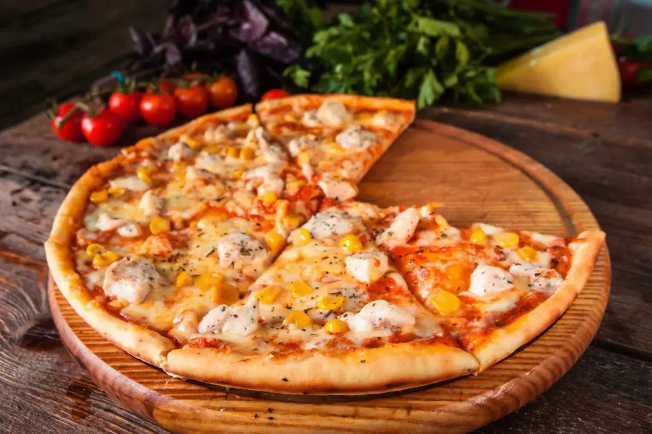 Pyszna pizza z kurczakiem i kukurydzą, podana na drewnianej desce, z pomidorkami i serem w tle.