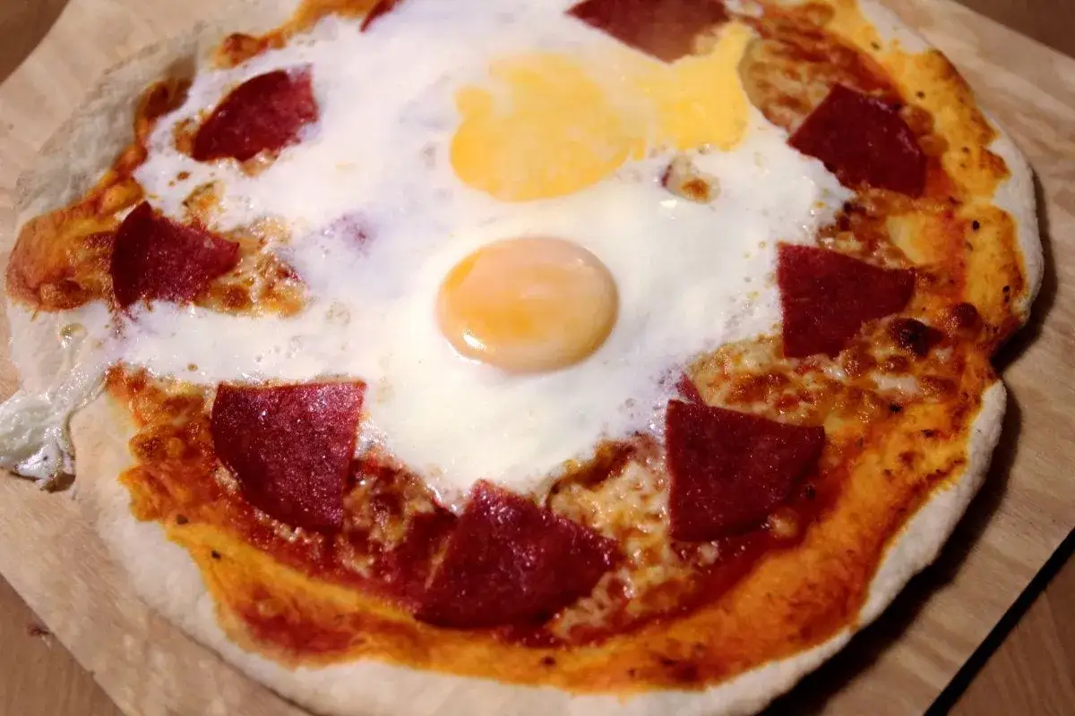 Pyszne ciasto na pizzę z jajkiem i salami, zapieczone na chrupiącym cieście. Idealne na śniadanie lub szybki lunch.