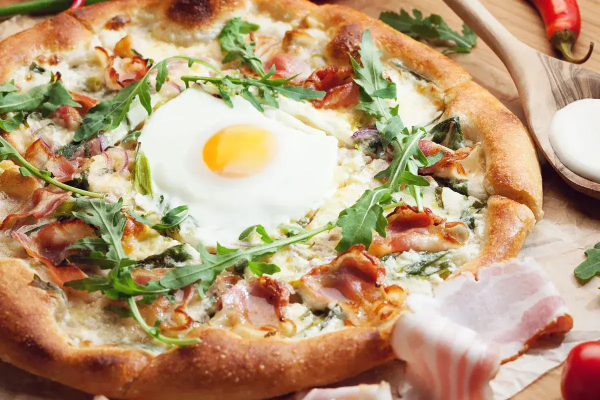 Pyszna pizza z jajkiem sadzonym, chrupiącym boczkiem i rukolą. Idealna na śniadanie lub brunch.