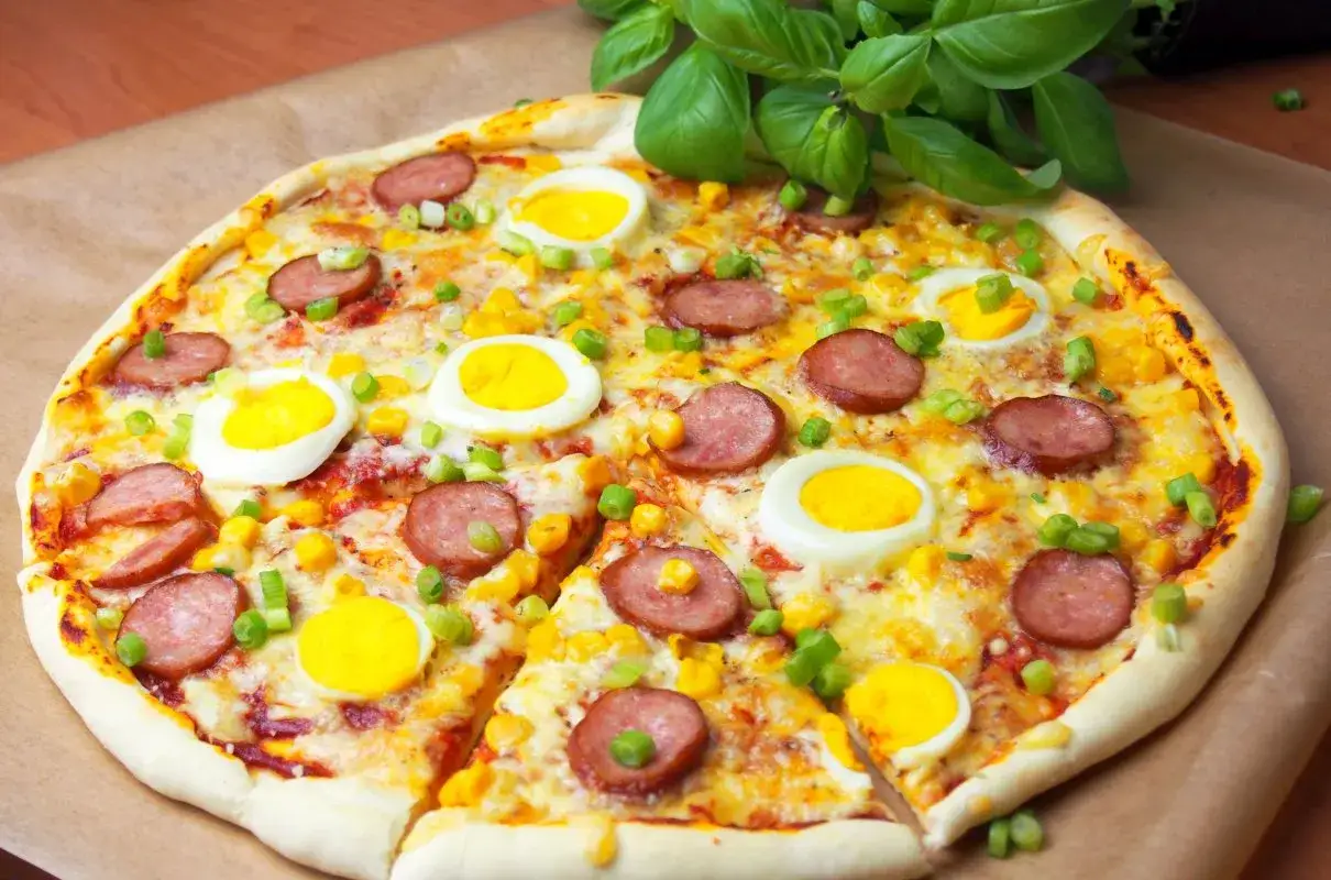Pyszne ciasto na pizzę z jajkiem, kiełbasą i kukurydzą, posypane szczypiorkiem. Idealna na śniadanie lub szybki obiad.