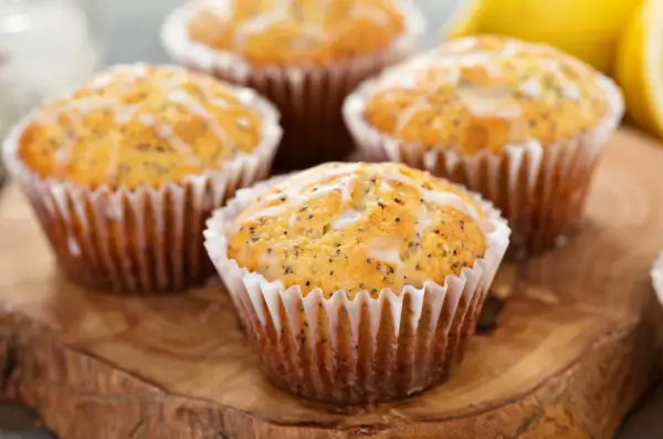 Cztery muffinki cytrynowe na oleju, posypane makiem i polane lukrem, prezentują się apetycznie na drewnianej desce.