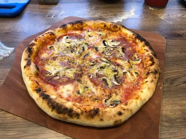 Pyszna pizza na drewnianej desce, idealnie wypieczona. Zastanawiasz się, ile nagrzewa się kamień do pizzy, by uzyskać taki efekt?